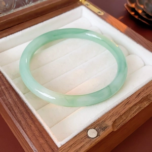 Macro detail of natural light green jade bangle with smooth round bar on wooden box