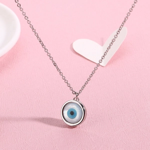 Silver titanium steel necklace featuring a blue evil eye pendant on a pink texture surface