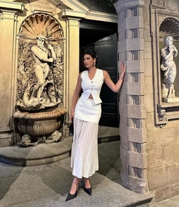 Détail de l'ensemble gilet blanc et jupe longue plissée devant une fontaine