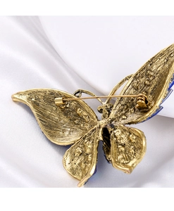Détail de l'arrière d'une broche papillon dorée avec épingle sur soie blanche