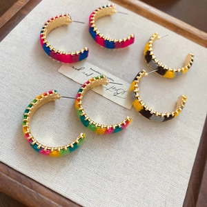 Macro shot of three colorful knitted C-shaped hoop earrings on a canvas jewelry tray