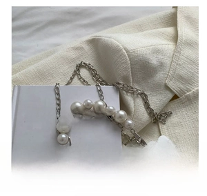 Detail of silver chain strap woven with gradient white pearls on textured suit