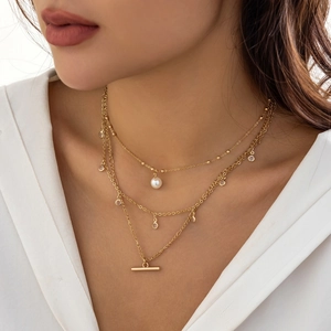 Close-up of triple-layered gold necklace with pearls and zircon charms on a model