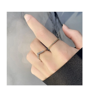 Gros plan d'une bague dorée pavée et d'un anneau argenté en V portés sur une main