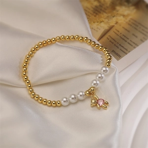 Detailed close-up of golden beads and pearl bracelet with a pink gemstone bear charm