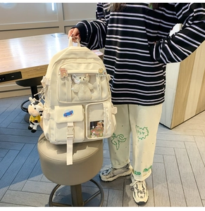 Dettaglio dello zaino bianco sporco con spille di cartoni e un ciondolo a forma di mucca