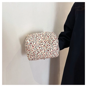 Close-up of quilted floral makeup bag with red flowers held against a white wall