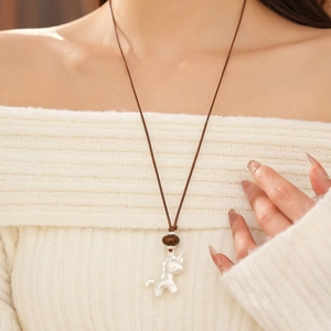 Gros plan du pendentif licorne argent mat avec cordon tressé brun sur un pull crème