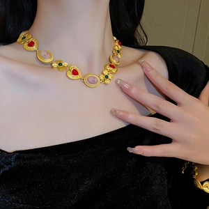 Detalle de collar vintage dorado con gema de corazón rojo y colgante de camafeo rosa