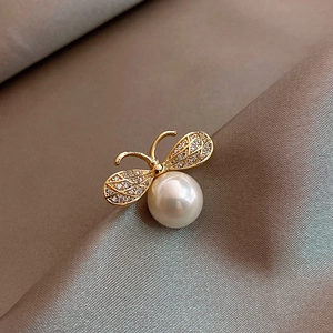 Macro shot of gold bee brooch with sparkling crystals and a large pearl on silk fabric