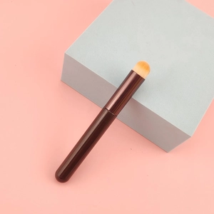 Close-up of a bullet-shaped concealer lip brush with orange bristles and a brown handle