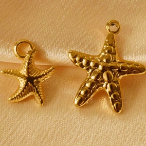 Detailed macro view of two golden starfish pendants in different sizes on silk fabric