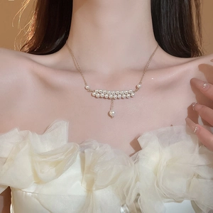 Close-up of double-layer faux pearl necklace with gold tassel on a white floral dress