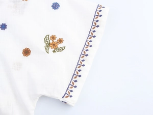 Close-up of intricate floral embroidery and cotton-linen texture on white shirt sleeve