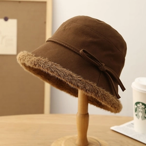 Deep brown plush bucket hat with faux fur trim and bow detail on wooden stand