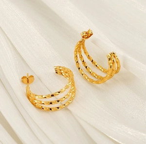 Macro shot of gold-plated triple-layered twisted C-shaped earrings on soft white fabric