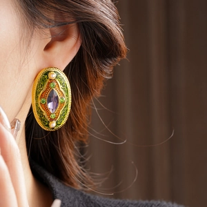 Close-up of vintage gold oval earrings with green enamel, purple stone and white pearls