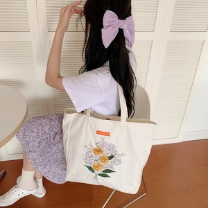Detailed close-up of yellow and purple floral embroidery on a white canvas tote bag