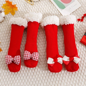 Festive red baby Christmas socks with lamb wool trim and decorative bows on knit rug