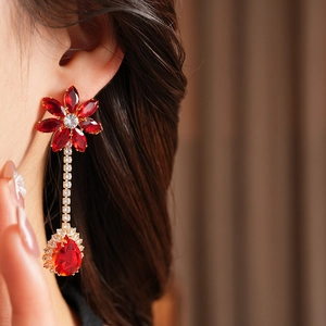 Close-up of red flower drop earrings with golden metal and sparkling gemstone tassels