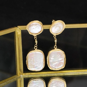 Elegant gold baroque pearl drop earrings featuring handcrafted wire on a mirror stand
