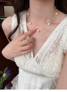 Detail of French vintage pearl necklace with golden chain worn on model with lace dress