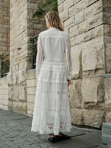 Detailed back view of long-sleeved white lace maxi dress against European stone background