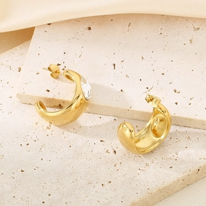 Detail of gold-plated C-shaped stud earrings with sparkling zircon on stone background