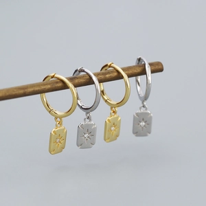 Macro detail of gold and silver S925 geometric earrings with starburst pendants