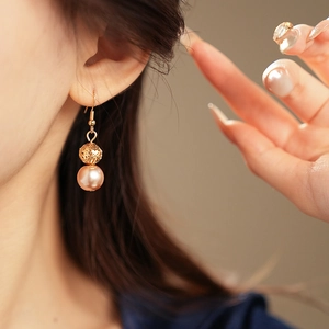 Close-up of elegant gold hollow sphere earrings with pink pearls on female model