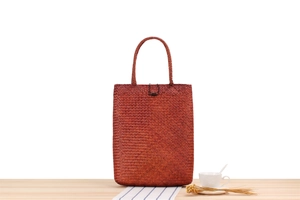 Detail of a brown woven straw handbag with a wooden button on a rustic wooden table
