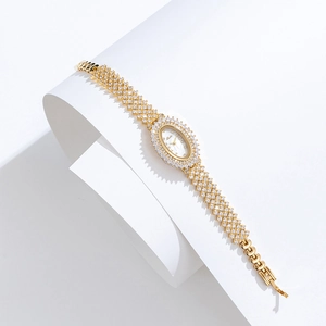 Detail of elegant gold oval watch with crystal diamonds and mesh bracelet on white artistic set
