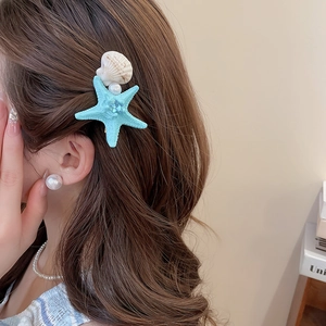 Detail of star pearl shell hair clip and earrings worn on wavy hair for a beach look