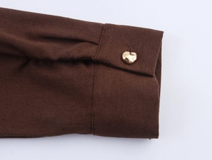 Macro shot of dark brown fabric cuff featuring a polished gold heart-shaped metal button