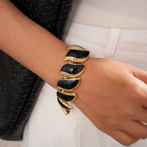 Gros plan du bracelet vintage aux feuilles noires bordées d'or sur le poignet d'un mannequin