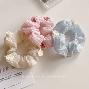 Three elegant fabric camellia flower scrunchies in pink, blue, and beige colors