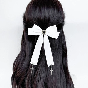 Détail d'une pince à cheveux nœud blanc avec cœur noir et pendentifs croix argentés