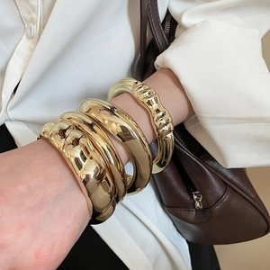 Gros plan de quatre bracelets joncs dorés épais avec finition miroir polie au poignet