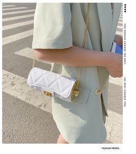 Close-up of white quilted mini cylinder bag with gold chain strap on a street model