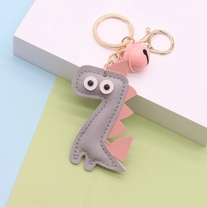 Detail of grey PU leather dinosaur keychain with pink accents and golden bell