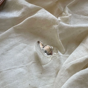 Detailed view of silver 925 heart ring with molten lava texture on cream linen fabric