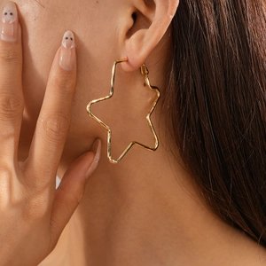 Close-up of a model wearing large gold hollow star-shaped metal hoop earrings