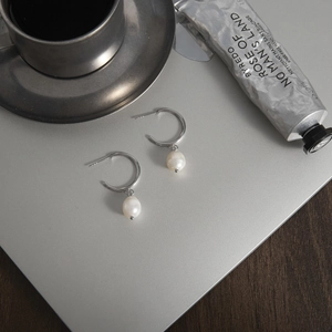 Silver stainless steel hoop earrings with elegant white pearl charms on metallic surface