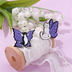 Macro detail of enamel cat pins featuring purple butterfly wings on a soft pastel background
