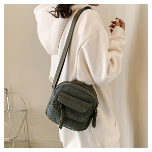 Detail of dark green corduroy crossbody bag showing texture and woven zipper pull