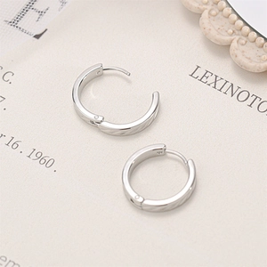 Detailed close-up of polished silver titanium steel hoop earrings on artistic paper