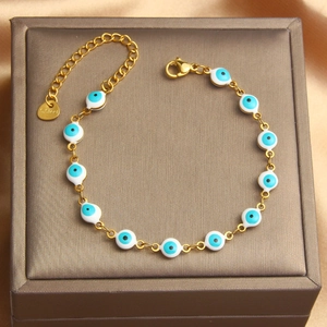 Close-up of golden stainless steel bracelet featuring colorful evil eye beads on satin