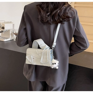 Détail d'un sac bandoulière en cuir clair avec poignée nouée et breloque peluche sur mannequin