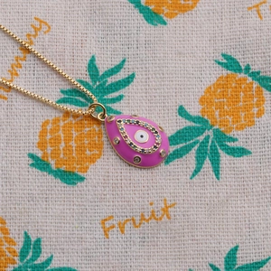 Close-up of gold chain necklace with pink enamel evil eye pendant and colorful stones