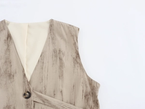 Dettaglio del gilet con scollo a V, bottone tartarugato e trama marrone su tessuto di lino